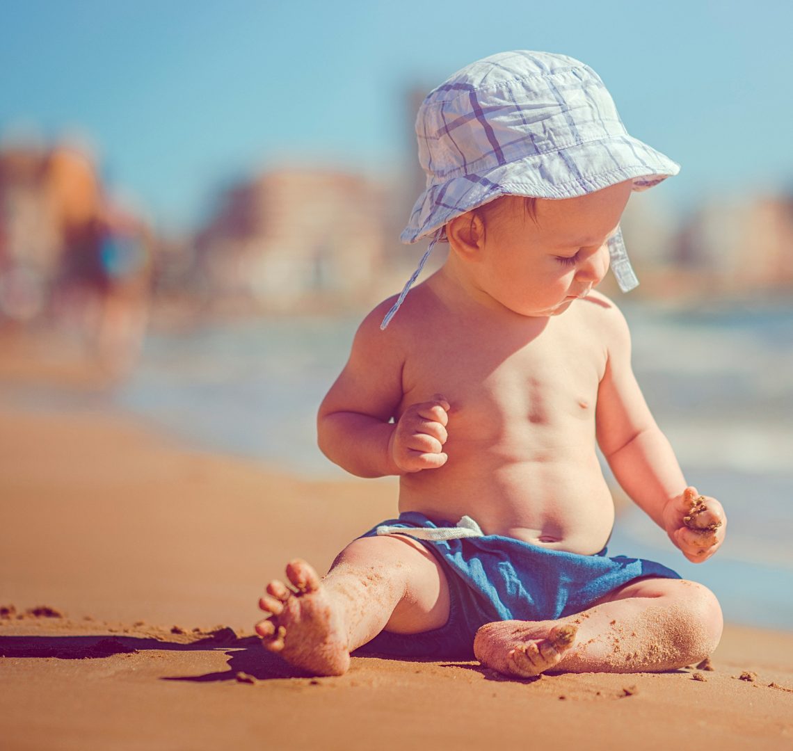 A baby in a sun hat studying the sand