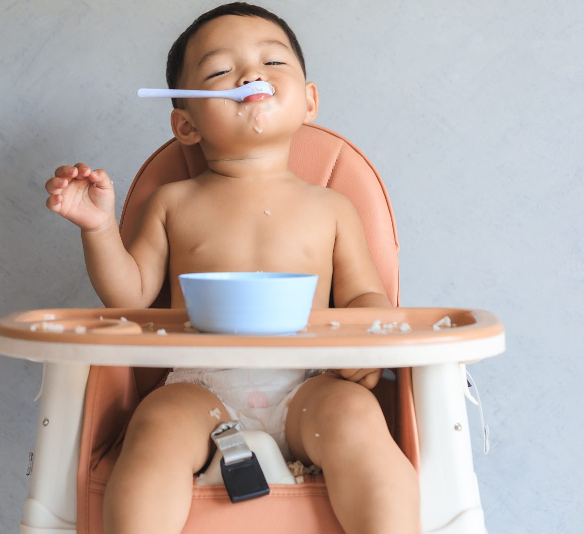 A baby in a high chair balancing a spoon on his nose